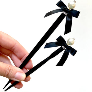 A full shot of the large and standard sizes of the Audrey Hair Stick made with ivory glass pearl beads and a classic black satin bow.