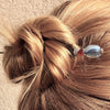 A blonde woman wears a messy bun using the Charlotte Tidal Hair Stick made from red white and blue swirl glass beads