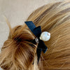 A woman wears one of the Audrey Hair Sticks made with ivory glass pearl beads and a classic black satin bow.