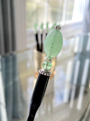 A close up of our handmade Remy hair sticks made from oval green swirl Czech glass beads. 
