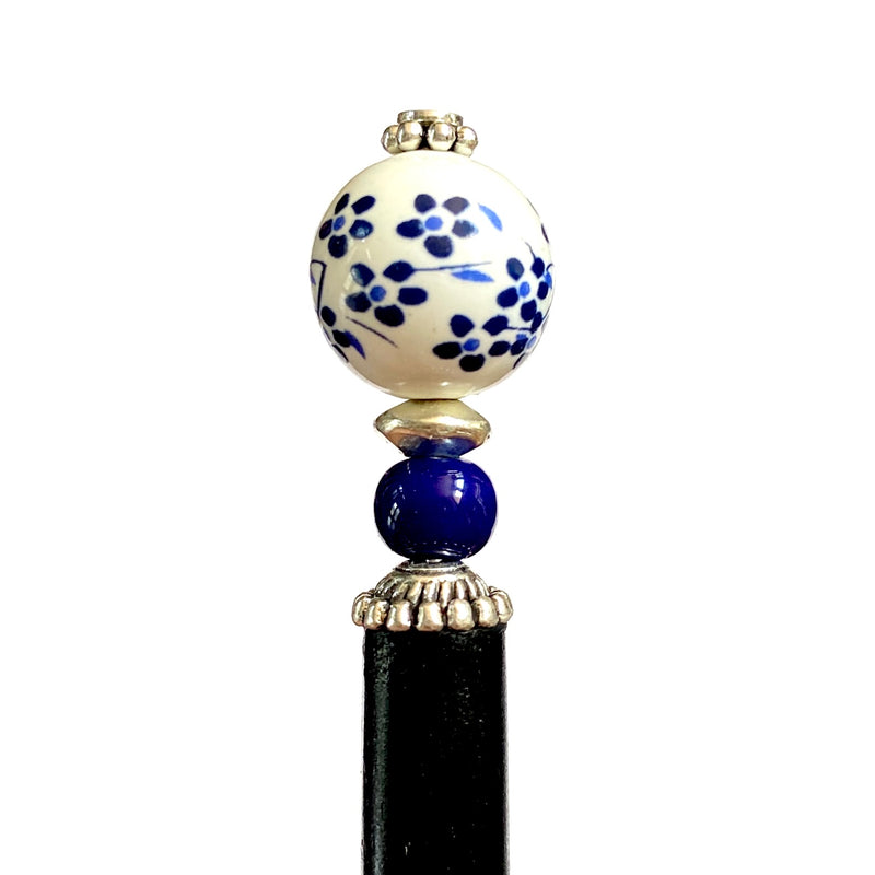 A close up of the Nora Tidal Hair Stick made from blue flowered white ceramic beads
