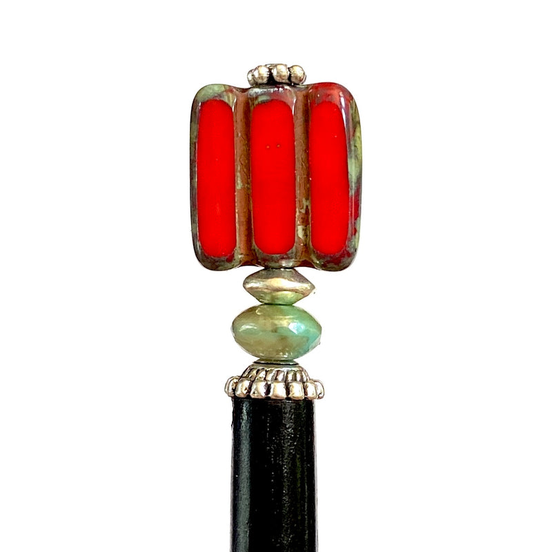 A close up of the Nela Tidal Hair Stick made from a red Czech glass bead