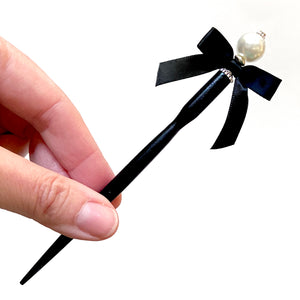 A full shot of the standard size of the Audrey Hair Stick made with ivory glass pearl beads and a classic black satin bow.