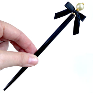 The large size of the Audrey hair stick made with an ivory glass pearl and black satin bow. 