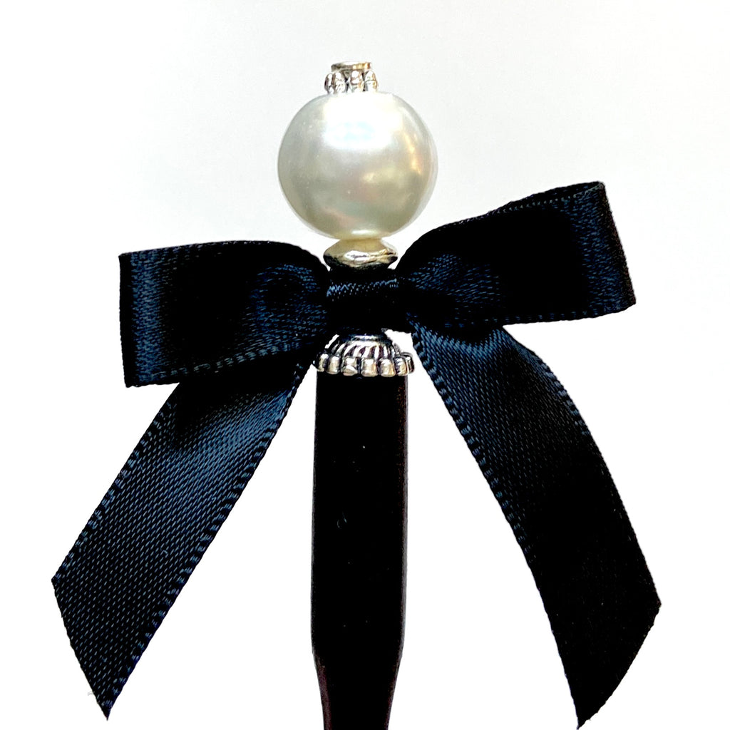 A close up of the Audrey Hair Stick made with ivory glass pearl beads and a classic black satin bow. 