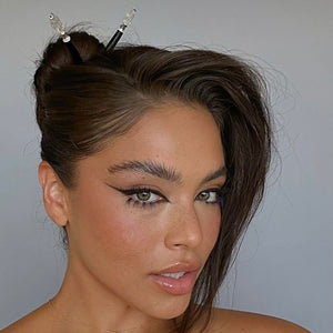 A brunette woman wears two Natasha hair sticks in her hair bun. 