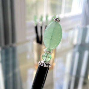 A close up of our handmade Remy hair sticks made from oval green swirl Czech glass beads. 