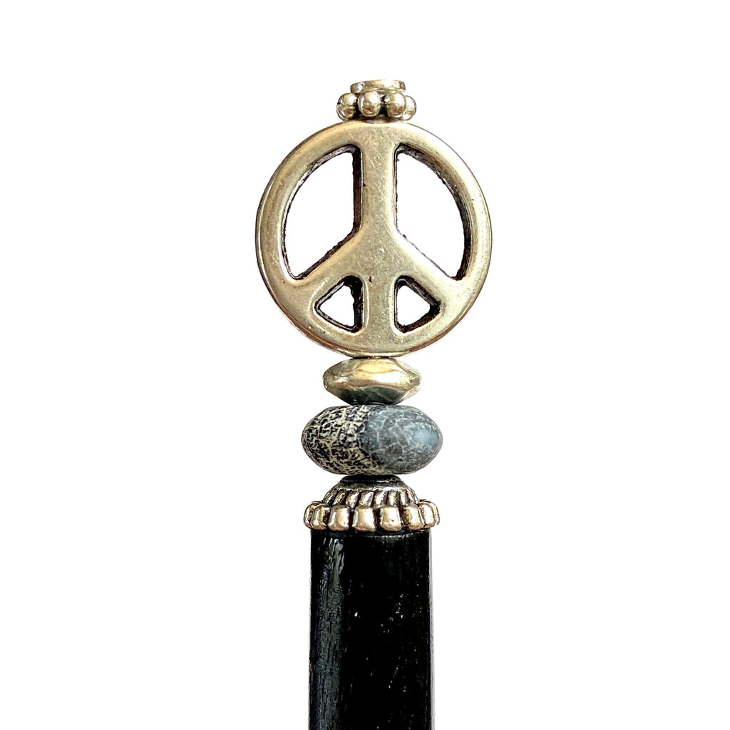 A close up of the Freedom Tidal Hair Stick made from a silver peace sign and denim-colored accent bead.