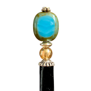 A close up of the Adelaide Tidal Hair Stick made of a blue Czech glass bead and wood base