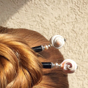 A woman wears two of the Cali Tidal Hair Sticks made from natural shell beads and pearl accent bead