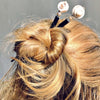 A blond woman wears a messy bun using two of the the Cali Tidal Hair Stick made from a natural shell bead and pearl accent bead