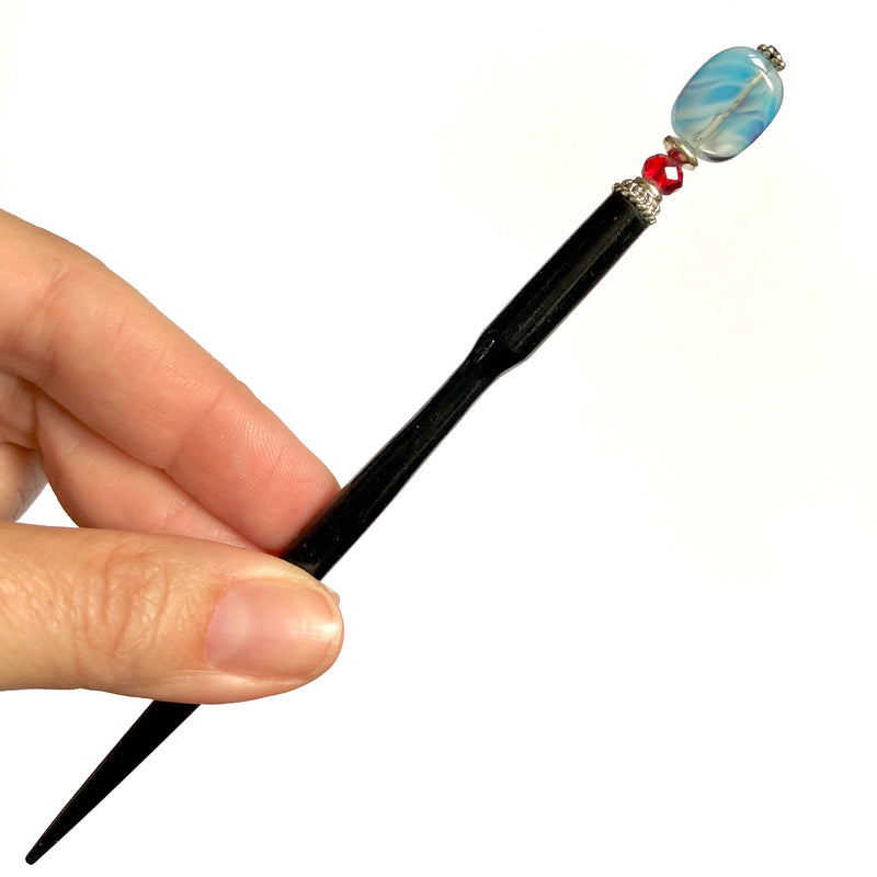 A close up of the Charlotte Tidal Hair Stick made from red white and blue swirl glass beads.