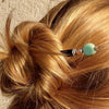 A blonde woman wears a messy bun using the Dakota Tidal Hair Stick made from a turquoise Czech glass bead,