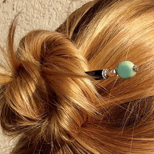 A blonde woman wears a messy bun using the Dakota Tidal Hair Stick made from a turquoise Czech glass bead,