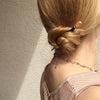 A blonde woman wears a low bun secured with the Ellen Hair Stick made from blush pink peach African Recycled Glass beads.