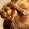 A blonde woman wears a hair bun with the Ellen Hair Stick made from blush pink peach African Recycled Glass beads.