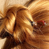 A blonde woman wears a messy bun with the Eve Tidal Hair Stick made from pink mother of pearl shell beads.