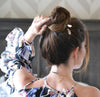 A millennial woman wears two of the Eve Tidal Hair Stick made from pink mother of pearl shell beads.