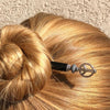 A blonde woman weras a hair bun using the Freedom Tidal Hair Stick made from a silver peace sign and denim-colored accent bead.