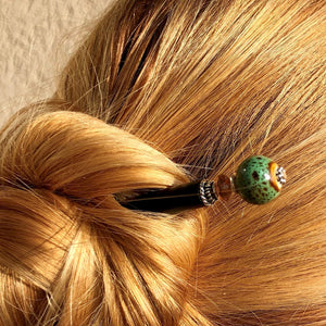 A blonde woman wears a hairbun using the Harlow Tidal Hair Stick made from green raku fired ceramic beads.