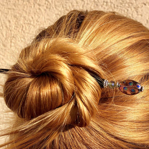 A blonde woman wears a messy bun using one of the Juno Tidal Hair Sticks made from purple Czech glass beads.