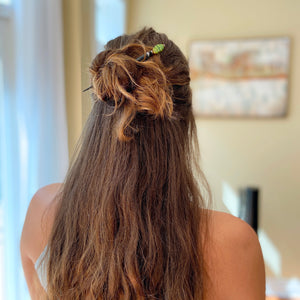 A woman wears one of our Kaja Hair Stick made from green swirl Czech glass beads