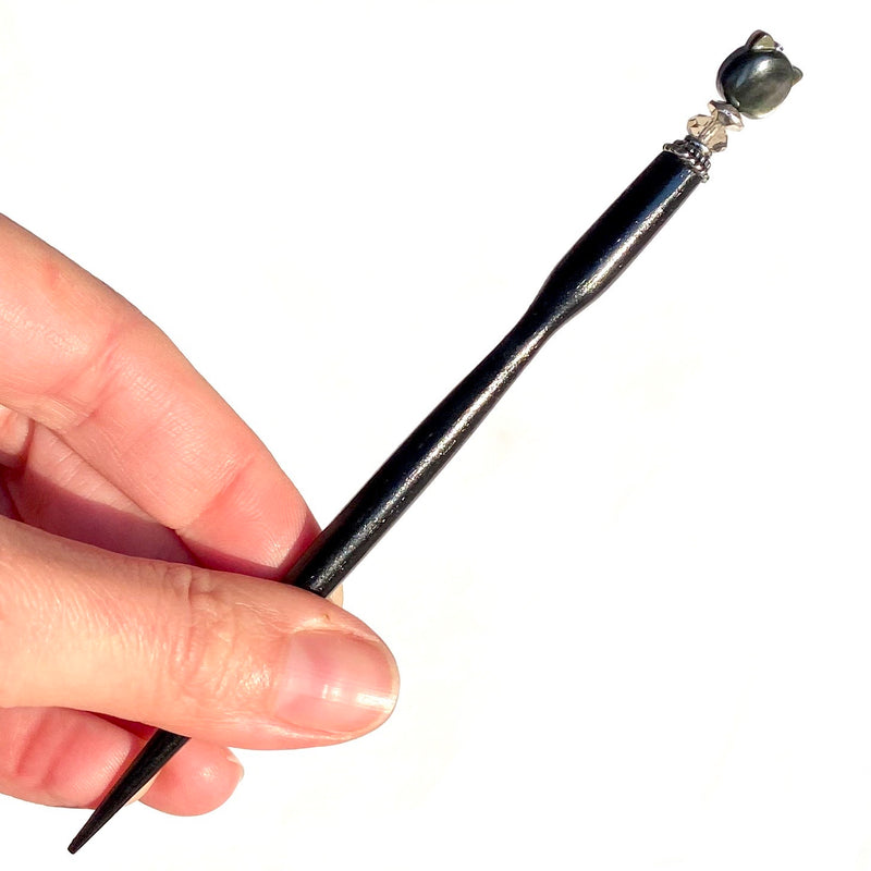 A close up of our Kat Hair Stick made from a black mother of pearl bead shaped like a cat head.
