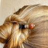 A blonde woman wearing one of of our Kennedy Hair Stick made from copper-colored goldstone.