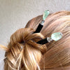 A woman wears two of the Kira Tidal Hair Sticks made from green fluorite stones.