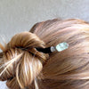 A woman wears one of the Kira Tidal Hair Sticks made from green fluorite stones.