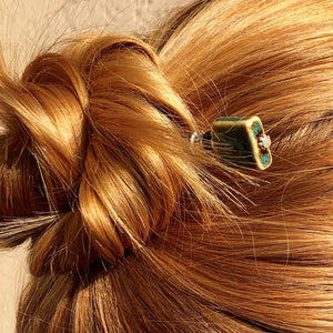 A blonde woman wears a messy bun using the Lark Tidal Hair Stick made from square blue raku fired ceramic beads.