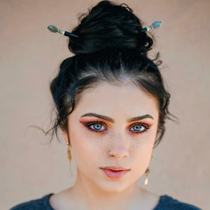 A woman wears two A close up of the Malia Tidal Hair Stick made from gray Labradorite stone beads.