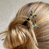 A blonde woman wears two  of the Mariposa Hair Sticks made from cloisonne butterfly beads