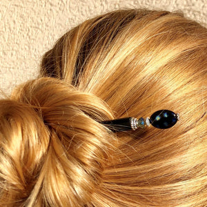 A blonde woman wearing a hair bun with the Melanie Tidal Hair Stick made from black Czech glass beads.