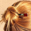A blonde woman wears a messy bun using the Nela Tidal Hair Stick made from a red Czech glass bead.