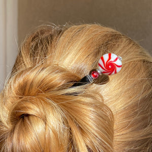 A woman wearing on of our Noelle Hair Stick made from a glass bead that looks like peppermint candy.