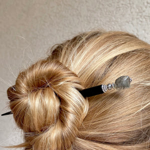 A woman wearing a hair bun using one of our Palmer Hair Sticks made from black rutile quartz stone.