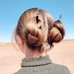 A woman wears two Palmer Tidal Hair Sticks in her spacebuns.  