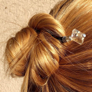 A blonde woman wears a messy bun with the Penelope Tidal Hair Stick made from iridescent clear glass beads.