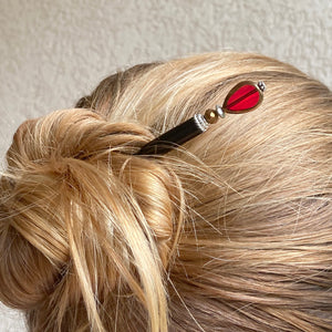 A woman wearing a hair bun with one of our Reina Hair Stick made from a red Czech glass bead with bronze edging.