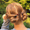 A woman wearing a hair bun using two of our Reina Hair Stick made from a red Czech glass bead with bronze edging.