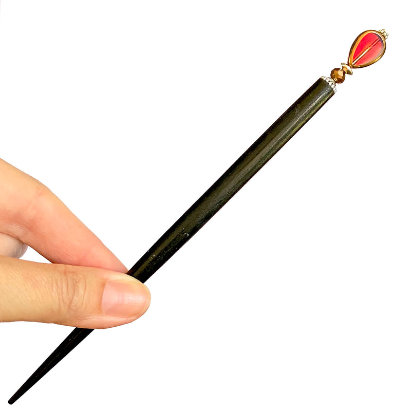 A close up of our Reina Hair Stick made from a red Czech glass bead with bronze edging