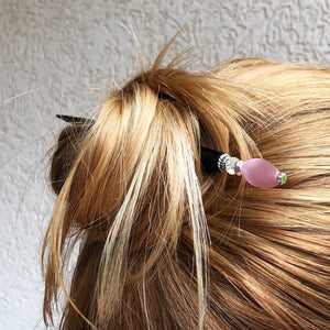 A woman wearing a messy bun with the Roxy Tidal Hair Stick made of pink cat's eye glass.