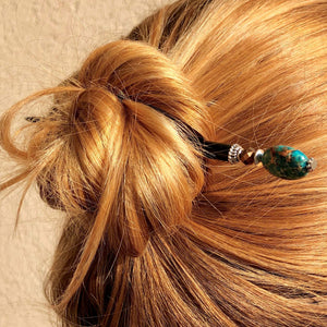 A woman wears a messy bun using the Terra Tidal Hair Stick made from blue Jasper stone beads.