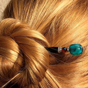 A woman wears her hair in a bun using the Zara Hair Stick made from teal blue and red swirl Czech glass beads.