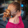A brunette woman wears a hair bun with two Zara Tidal Hair Sticks.