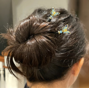 A brunette woman wears two Mariposa Hair Sticks