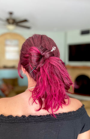A pink-haired woman wears a Freedom Tidal Hair Stick made from a silver peace sign and denim-colored accent bead