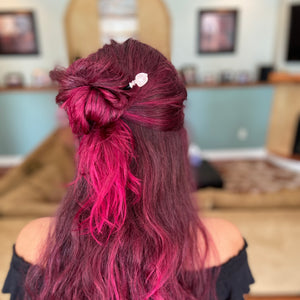 A woman with pink hear wears a Riley Hair Stick in her half-up hair bun.