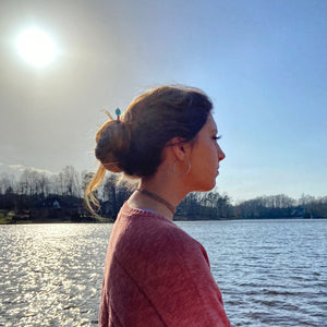 A woman is standing by a lake with a Zara Hair Stick in her hair bun.